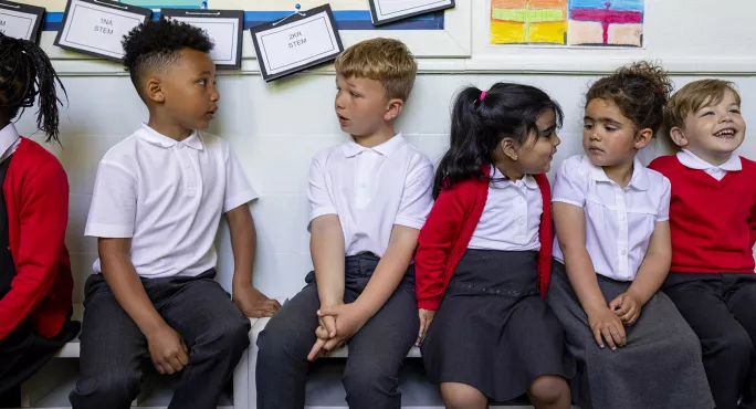Primary school children sit along a bench