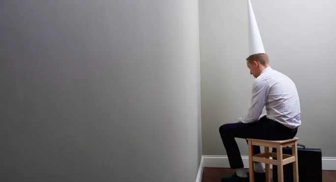 Man In Suit, Sitting In The Corner, Wearing A Dunce's Cap