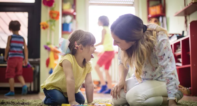 An Early-years Teacher Kneeling On The Floor With A Small Child