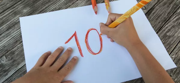 Children's Hands Writing '10' On Piece Of Paper