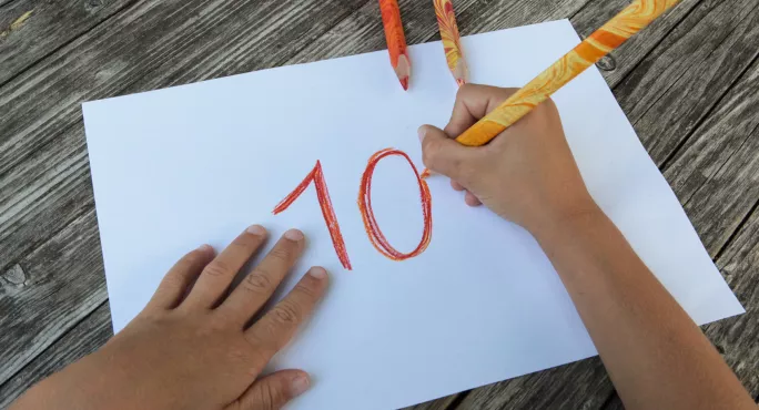 Children's Hands Writing '10' On Piece Of Paper