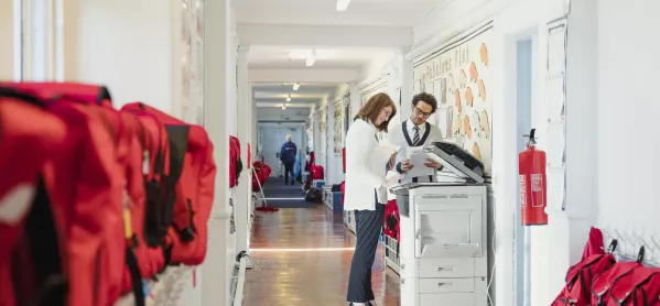 Teachers Using Photocopier In School Corridor