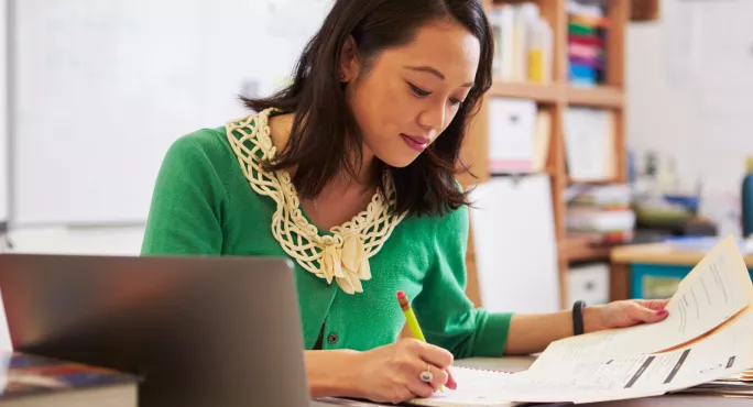 Teacher Sitting At Desk, Writing School Reports