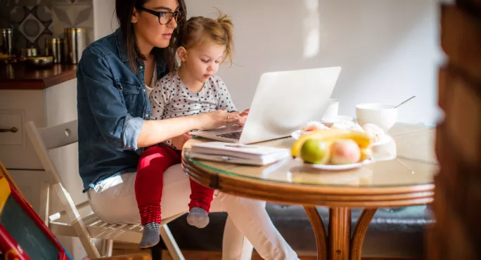 Woman Attempts To Work On Computer, While Holding Toddler On Her Lap