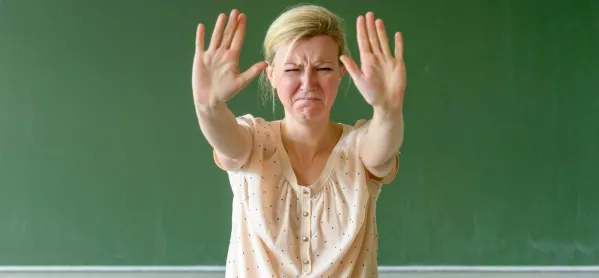 Upset Teacher Stands In Front Of Blackboard With Her Hands In The Air, To Indicate "stop"