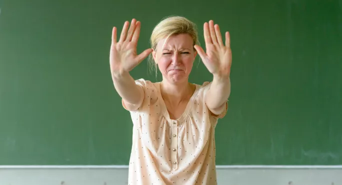 Upset Teacher Stands In Front Of Blackboard With Her Hands In The Air, To Indicate "stop"