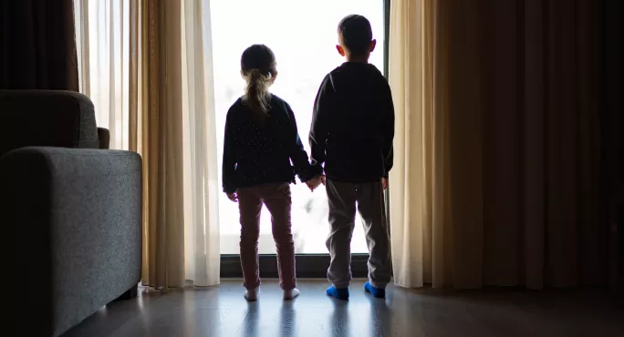 Two Small Children, Standing By A Window