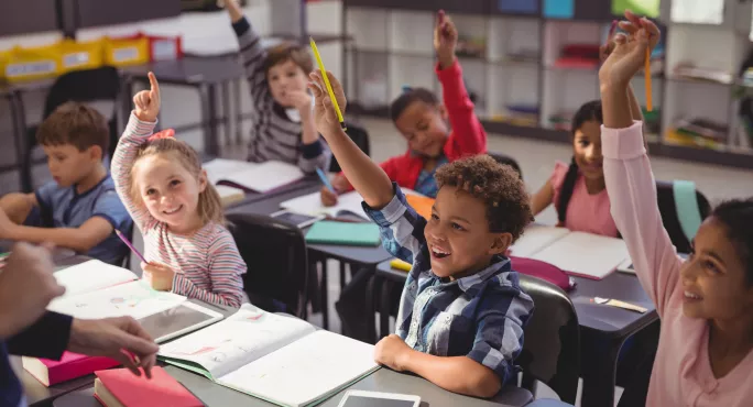 Children With Their Hands Up In Primary Class