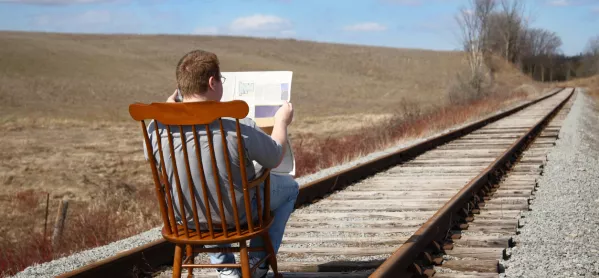 Man, Sitting Reading A Newspaper In The Middle Of Train Tracks