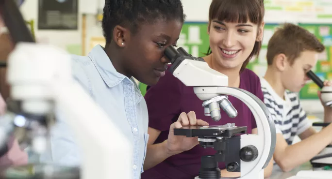 Student Looking Down A Microscope, Teacher Supporting Students In Science