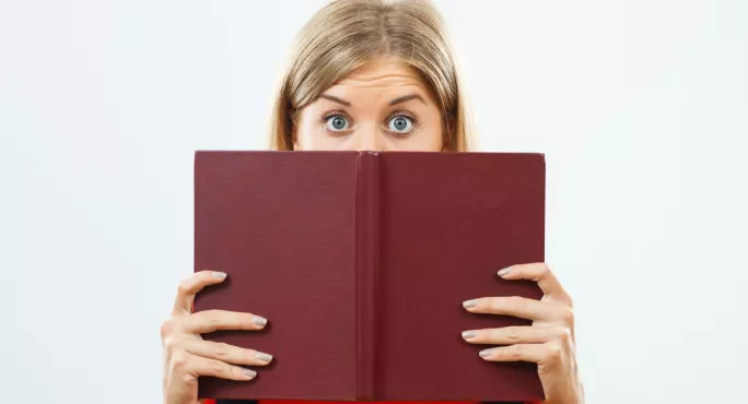 A Woman Gazes, Wide-eyed, Over The Cover Of A Book