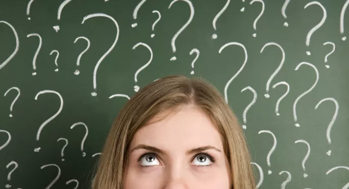 Woman Standing In Front Of Blackboard, On Which Question Marks Are Drawn