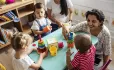 Nursery children sat round table with teacher playing with building blocks 