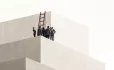 A small group of people trying to climb a wall using a ladder