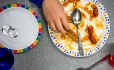 A person is eating from a plate of half-eaten toast and beans, with another plate with two silver coins on next to it 