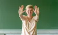 Upset Teacher Stands In Front Of Blackboard With Her Hands In The Air, To Indicate "stop"